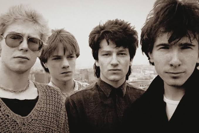 Sepia photograph of four young men standing on a rooftop above a city